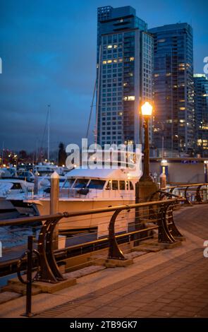 Gros plan des bateaux amarrés dans la marina et la promenade de la promenade illuminée par un lampadaire avec des gratte-ciel en arrière-plan au front de mer de ... Banque D'Images