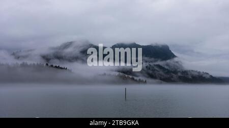 Vue imprenable depuis la marche le long de la digue du lac Pitt à Maple Ridge d'un sommet de montagne couvert d'un brouillard brumeux par un jour gris Banque D'Images