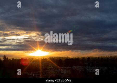 Un éclat de soleil éclatant traverse les nuages de tempête au-dessus d'une forêt et d'une ville découpées ; Surrey, Colombie-Britannique, Canada Banque D'Images