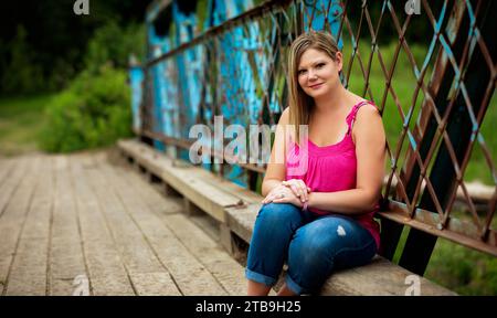 Portrait rapproché d'une femme assise sur un banc en bois le long d'un pont à chevalets lors d'une promenade dans la nature dans un parc, posant pour la caméra Banque D'Images