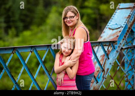 Portrait d'une mère et sa fille debout sur un pont à chevalets embrassant et regardant la caméra, alors que sur une promenade dans la nature dans un parc Banque D'Images