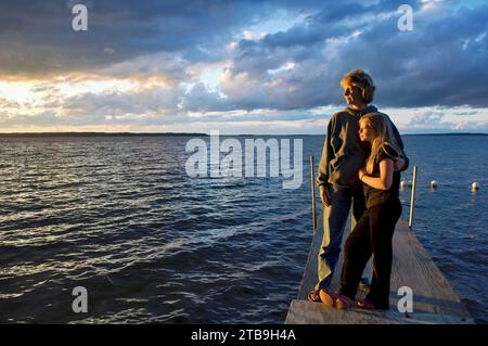 Mère et sa fille debout sur un quai de bateau regardant le coucher du soleil, lac Leech dans le Minnesota, États-Unis ; Walker, Minnesota, États-Unis d'Amérique Banque D'Images