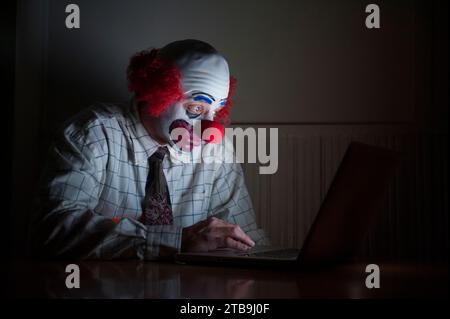 Clown portant une chemise et une cravate utilise un ordinateur portable pour surfer sur le web, ayant un regard large de surprise sur son visage Banque D'Images