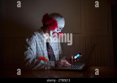 Clown portant une chemise et une cravate utilise un ordinateur portable et un téléphone intelligent simultanément ; Lincoln, Nebraska, États-Unis d'Amérique Banque D'Images