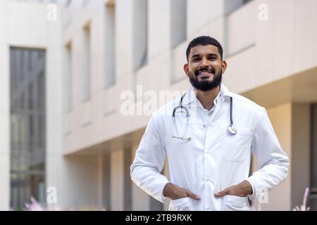 Portrait d'un médecin, infirmier, vétérinaire latino-américain debout à l'extérieur de la clinique dans la rue dans un manteau blanc et souriant et regardant avec confiance la caméra. Banque D'Images