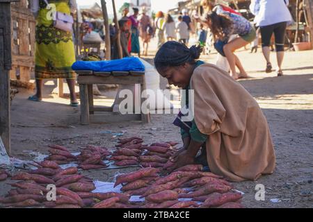 Ilakaka, Madagascar - 30 avril 2019 : femme malgache inconnue s'accroupant au sol, arrangeant des légumes à tubercules ou de la patate douce vendus au légume de rue Banque D'Images