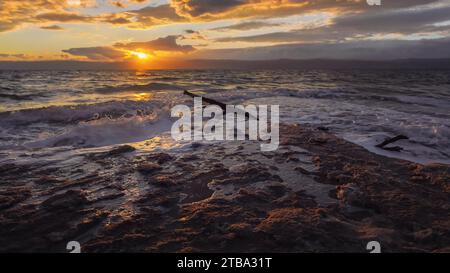 Le soleil brille à travers les nuages spectaculaires du coucher du soleil aux vagues du côté jordanien de la mer Morte, sable de rivage recouvert de sel Banque D'Images