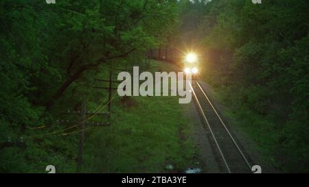 Le train de marchandises transportant du charbon traverse les forêts luxuriantes de l'Iowa alors que l'obscurité s'installe. Banque D'Images