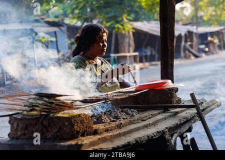 Jeune femme cuisinant du poisson sur un feu ouvert dans un marché de rue, près de Baucau, en République démocratique du Timor-Leste. Banque D'Images