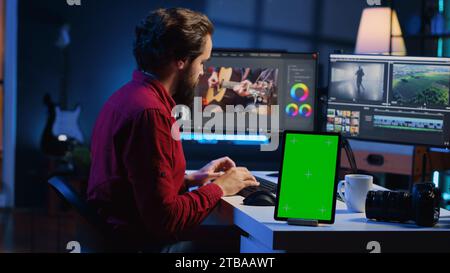 L'éditeur vidéo ajoute des effets sonores aux séquences filmées, travaillant en studio de post-production avec une tablette à écran vert. Vidéaste utilisant un casque pour tester et améliorer la qualité audio à côté du périphérique de maquette Banque D'Images