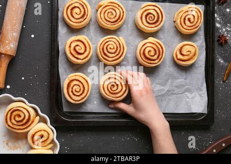 Femme préparant des rouleaux de cannelle sur fond noir Banque D'Images