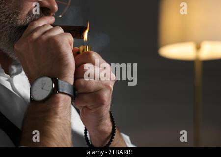 Homme barbu allumant un cigare à l'intérieur, gros plan. Espace pour le texte Banque D'Images