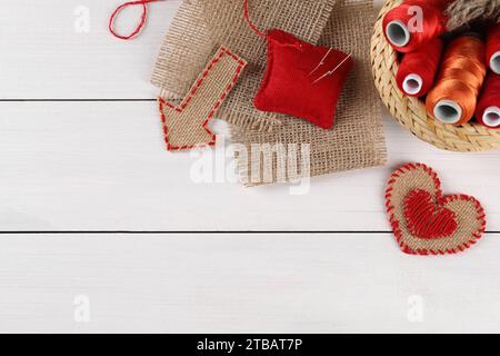 Morceaux de toile de jute, bobines de fils, coussinet et aiguilles sur table en bois blanc, pose à plat. Espace pour le texte Banque D'Images