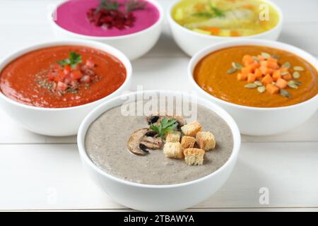 Bouillon savoureux et différentes soupes à la crème dans des bols sur la table en bois blanc, gros plan Banque D'Images