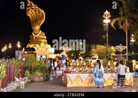 Image nocturne du Monument Naga, dévots en face, construit en 2016 à Nakhon Phanom, Thaïlande, présente une grande statue de serpent Naga en laiton à 7 têtes face au nord de l'autre côté du Mékong. Coûtant 9 millions de bahts, la sculpture mesure 4,49 mètres de large, 10,90 mètres de haut et pèse 9 tonnes. Nommée Phaya si Sattanakharat, elle est considérée comme la plus grande sculpture Naga en laiton du nord-est de la Thaïlande. Le Naga, au cœur de la mythologie thaïlandaise et du bouddhisme, a joué un rôle crucial dans la protection du Bouddha pendant l'illumination, comme dans l'histoire de Mucalinda, le Naga à 7 têtes. Banque D'Images