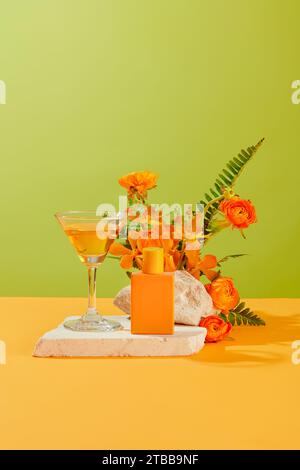 Un verre à cocktail contenant du liquide orange et une bouteille de parfum orange sont placés sur une plate-forme en pierre. Les fleurs fraîches sont liées en bouquets. Brillia Banque D'Images