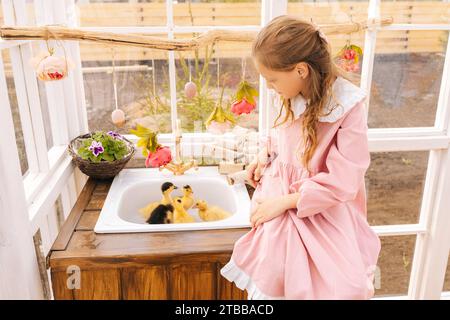 Portrait de mignonne petite fille portant une belle robe jouant avec de petits canetons jaunes s'installant sur le plancher de la maison gazebo d'été sur la journée ensoleillée. Banque D'Images