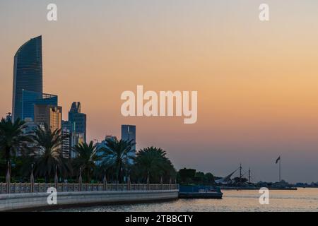 La corniche d'Abu Dhabi au coucher du soleil, gratte-ciel au loin, Émirats arabes Unis. Heure bleue, bâtiments modernes, mer perse. Banque D'Images