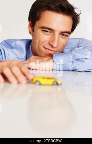 Homme, visage ou affaires avec voiture ou jouet pour penser, financer ou prêt de véhicule par table dans le bureau de l'entreprise. Personne, heureux ou moteur de rêve avec réfléchi Banque D'Images