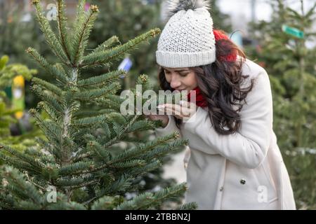 Une jeune femme sent les arbres de Noël fraîchement importés au marché. Banque D'Images