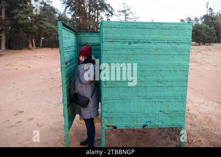 Une jeune femme habillée à la mode automnale à la mode communique par téléphone à partir d'une vieille cabine à langer patinée située sur un tranquille bea d'automne Banque D'Images