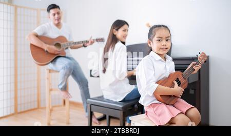 La famille se joint à jouer de la musique. Père joue de la guitare, mère joue du piano. Fille jouant de l'ukulele Banque D'Images