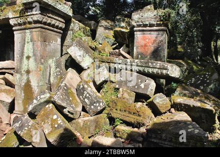 Écroulé des pierres de temple, certaines avec de la mousse et des sculptures couvertes de lichen empilées parmi les ruines antiques du parc archéologique d'Angkor au Cambodge. Banque D'Images