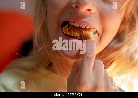 la fille mange un croissant en le bourrant dans sa bouche Banque D'Images