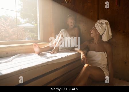 Mère et fille dans un sauna, mère avec une serviette sur la tête, souriante et assise Banque D'Images