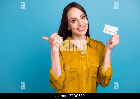 Photo de bonne humeur jolie fille habillée chemise jaune montant pouce carte de crédit espace vide isolé fond de couleur bleue Banque D'Images