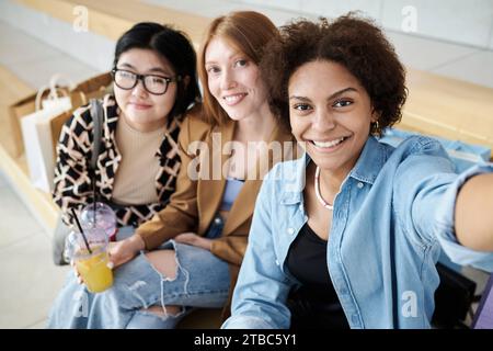 Groupe multiracial d'amis prenant selfie ensemble assis sur le banc au centre commercial Banque D'Images