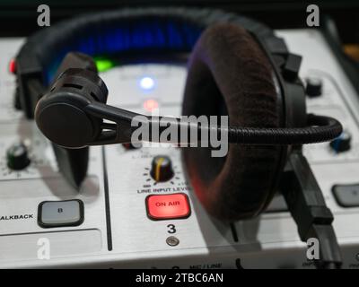 Gros plan d'une console de mixage avec un bouton lumineux sur l'air et un casque sur le lieu de travail d'un commentateur sportif Banque D'Images