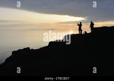 Un groupe de touristes prenant des photos d'un coucher de soleil sur l'Atlantique à Neist point sur l'île de Skye, en Écosse. Banque D'Images