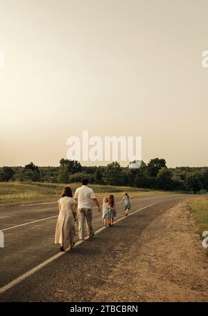 Maman, papa et filles marchent l'un après l'autre le long d'une route rurale le long de la forêt. Une famille heureuse Banque D'Images