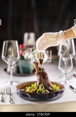 Le chef ou le serveur termine le repas directement sur la table du restaurant, en versant la sauce sur le gigot d'agneau confit. Banque D'Images