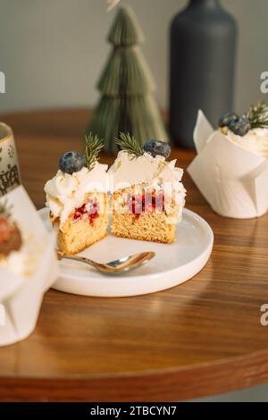 Demi-cupcakes avec garniture de fruits décorée de baies avec une branche d'arbre de Noël sur une assiette blanche Banque D'Images