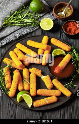 bâtonnets de mozzarella frits avec sauce, tranches de citron vert et romarin frais sur plateau noir sur table en bois noir, cuisine américaine, vue verticale Banque D'Images