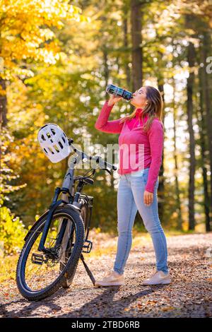 Femme sur la bouteille d'eau potable ebike dans la forêt d'automne, Forêt Noire, Gechingen, Allemagne Banque D'Images