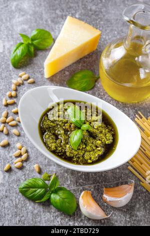 Sauce pesto maison dans un petit bocal en verre et ingrédients pour pâtes sur béton gris. Cuisine italienne traditionnelle, recette, menu du restaurant Banque D'Images