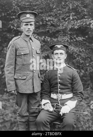 Portrait décontracté édouardien de deux hommes en uniforme, à l'extérieur, un assis et un debout. Pris à partir d'un négatif de plaque de verre vintage. C1900 – 1910 Banque D'Images