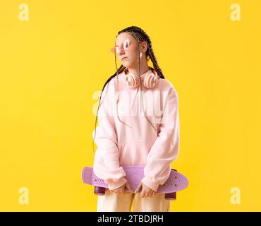 Jeune femme avec des dreadlocks et skateboard sur fond jaune Banque D'Images