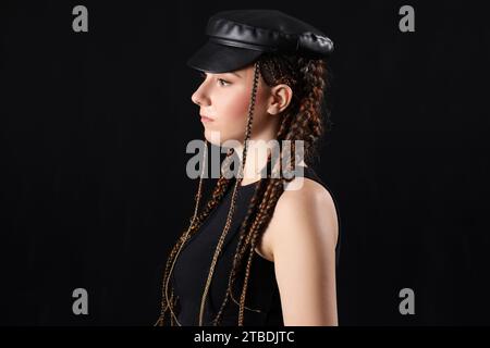 Jeune femme avec des dreadlocks dans un chapeau élégant sur fond sombre, closeup Banque D'Images