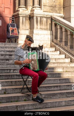 Paris, France - 01 septembre 2023 : musicien de rue joue de l'accordéon avec chat noir sur les escaliers de la basilique du Sacré-cœur à Montmartre Banque D'Images