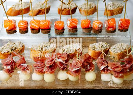 Une gamme luxueuse de canapés avec du saumon fumé, du melon enveloppé de prosciutto et du fromage sur du pain croustillant, magnifiquement disposés sur un plateau en verre Banque D'Images