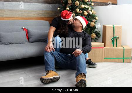 Couple d'homme latino-américain en surpoids à peau foncée et femme dans leurs années 30 profiter des vacances en couple à côté de l'arbre de Noël Banque D'Images