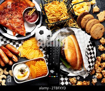 Graisses saturées. L'heure du football. Télécommande TV et collations - chips, pop-corn, biscuits, fromage, sauce, frites, burger, noix. Vue de dessus Banque D'Images