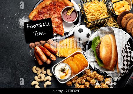 Graisses saturées. L'heure du football. Télécommande TV et collations - chips, pop-corn, biscuits, fromage, sauce, frites, burger, noix. Vue de dessus Banque D'Images