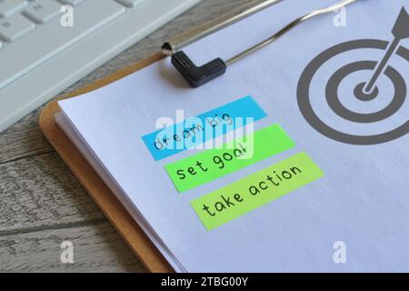 Image rapprochée du presse-papiers papier avec l'icône du tableau cible et le texte RÊVENT GRAND, DÉFINISSEZ L'OBJECTIF et PRENEZ DES MESURES. Concept de motivation. Banque D'Images