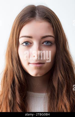 Jeune femme à la peau claire et une expression neutre se dresse sur un fond blanc, ses longs cheveux bruns encadrant son visage Banque D'Images