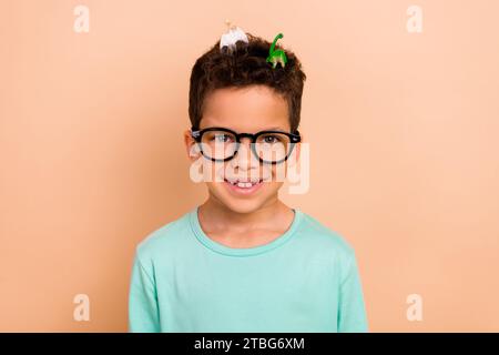 Photo de positif mignon gentil garçon porter des vêtements à la mode collectant des jouets de jeu petits dinosaures isolés sur fond de couleur beige Banque D'Images